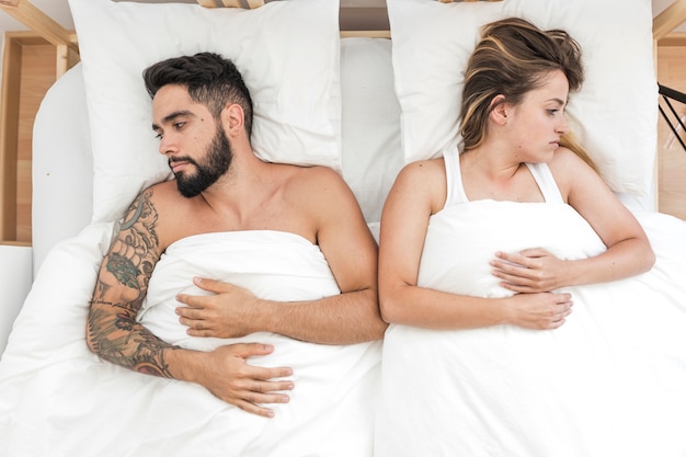 High angle view of sad couple lying on bed