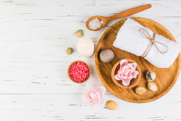 High angle view of salt; candle; spa stones; towel and flower on wooden backdrop