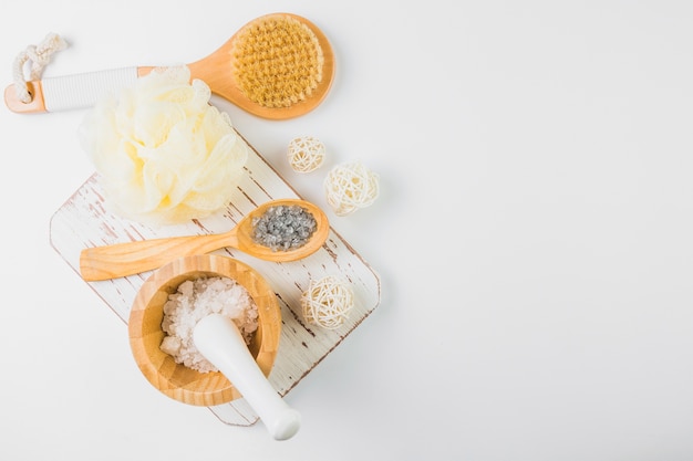 High angle view of salt; loofah and brush on white backdrop