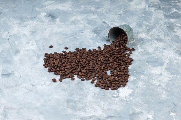 High angle view scattered coffee beans from cup on grey plaster background. horizontal