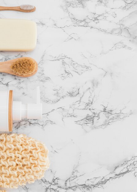 High angle view of scrub glove; cosmetic bottle; brush and soap on marble surface