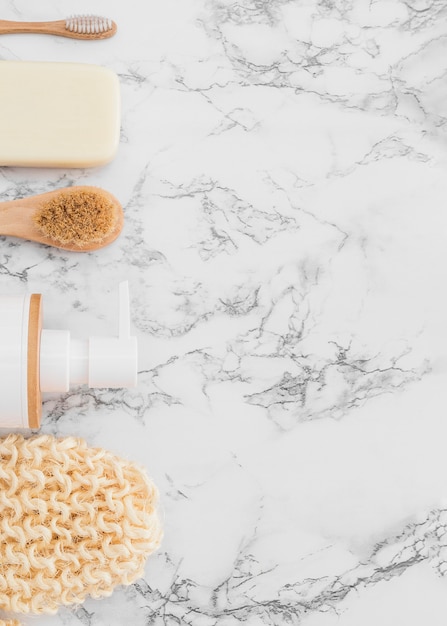 High angle view of scrub glove; cosmetic bottle; brush and soap on marble surface