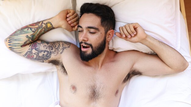 High angle view of a shirtless young man sleeping on bed