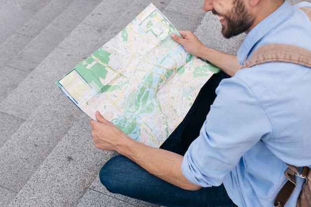 High angle view of smiling man sitting on staircase and reading map