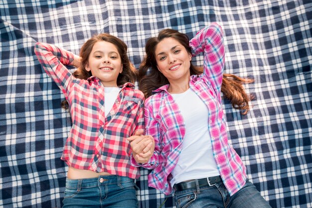 High angle view of smiling mother and daughter lying on checkered pattern blanket