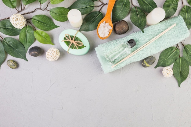 Free photo high angle view of spa stones; towel; salt; soap; leaves and candles on grey background