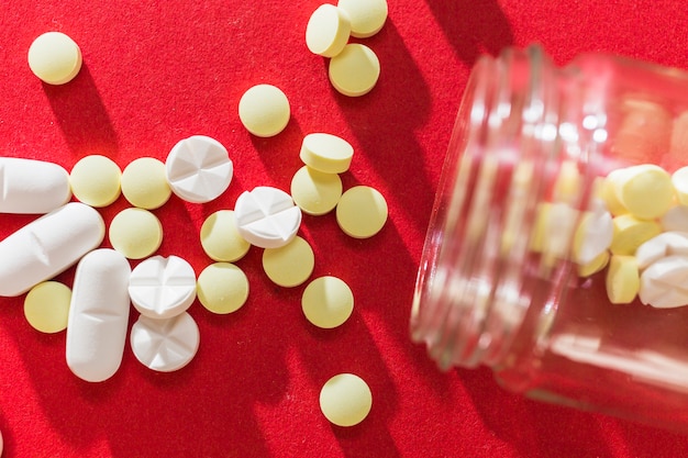 High angle view of spilled out pills from container on red background