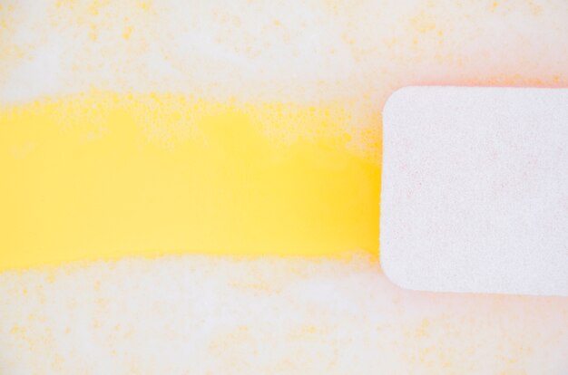 High angle view of sponge cleaning soap sud on yellow backdrop