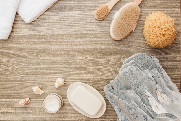 High angle view of sponge; seashell; soap; brush; towel and moisturizing cream on wooden backdrop