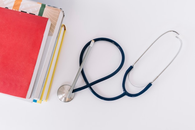 High angle view of stacked books and stethoscope on white surface