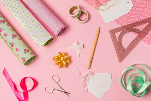 High angle view of stationery supplies with gift wrap and tags on pink background