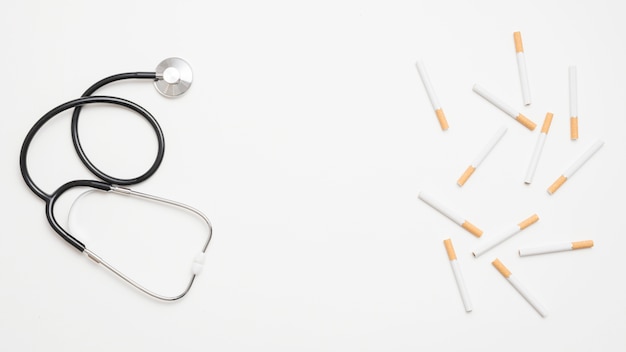 High angle view of stethoscope and cigarettes on white background