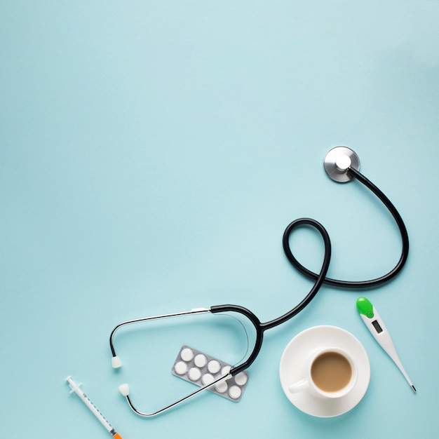 High angle view of stethoscope; coffee cup; tablets; thermometer; injection over blue desk