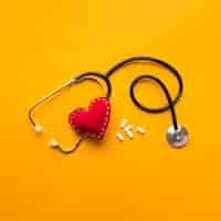 Free photo high angle view of stethoscope; stitched heart and medicines over yellow backdrop