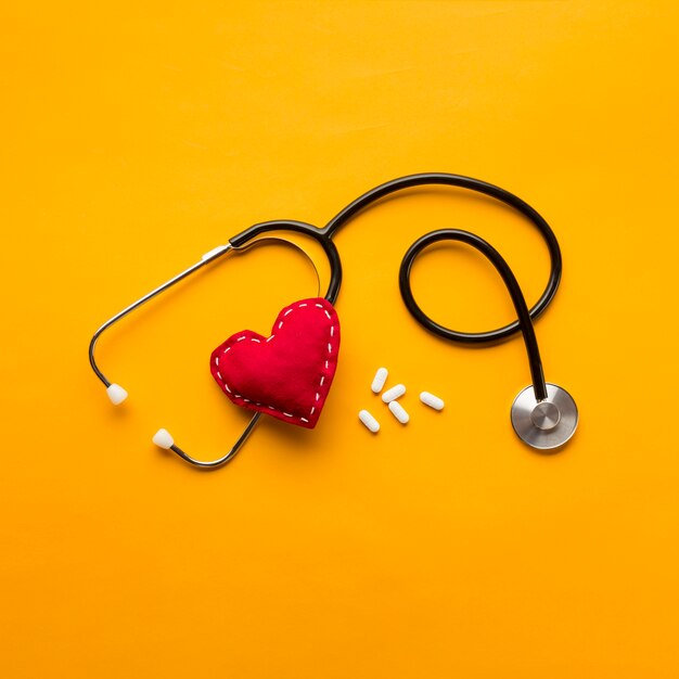 High angle view of stethoscope; stitched heart and medicines over yellow backdrop