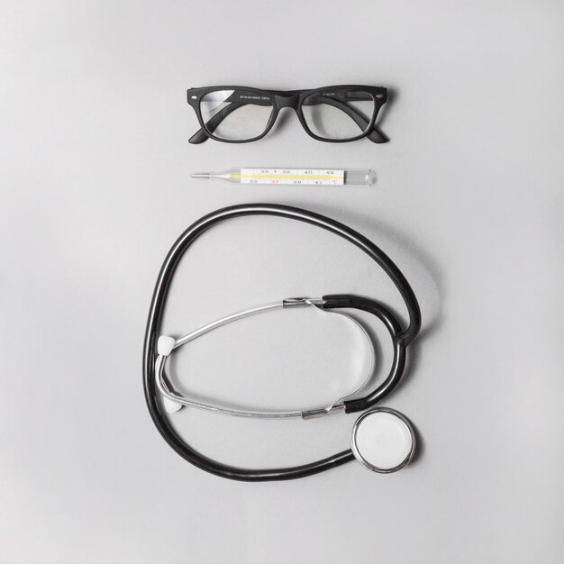 Высокий угол зрения стетоскопа; термометр и очки на сером фоне
