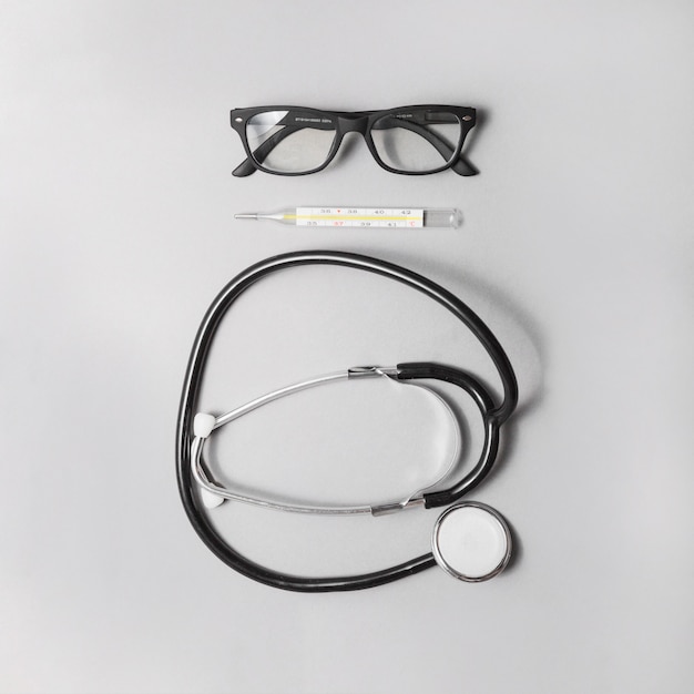 High angle view of stethoscope; thermometer and spectacles on grey background