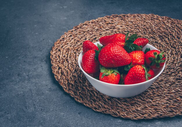 High angle view strawberries in bowl on trivet and gray textured background. horizontal