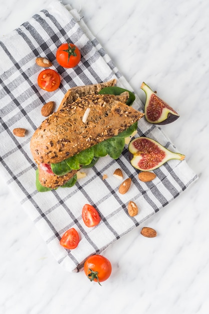 Free photo high angle view of tasty hot dog; fresh fig slices; almonds and cherry tomatoes on napkin over white backdrop