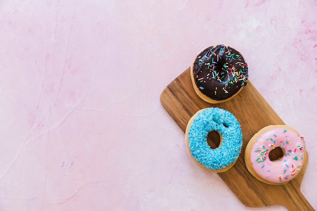 High angle view of three fresh donuts on wooden chopping board