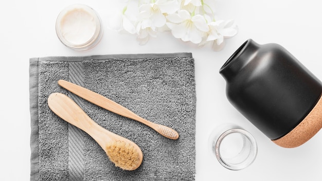high angle view of towel; brush; moisturizing cream; flowers and jar on white background