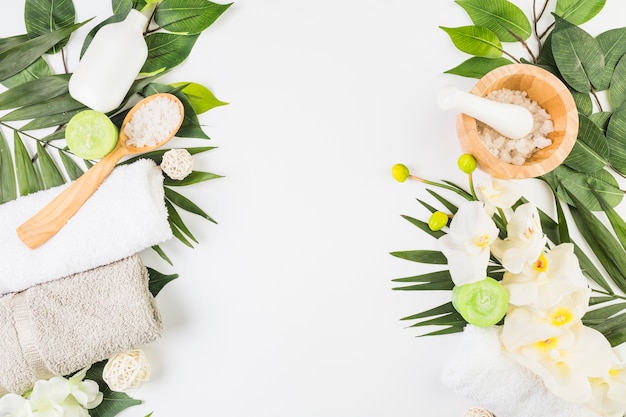 High angle view of towels; salt; candles; flowers and leaves on whit surface