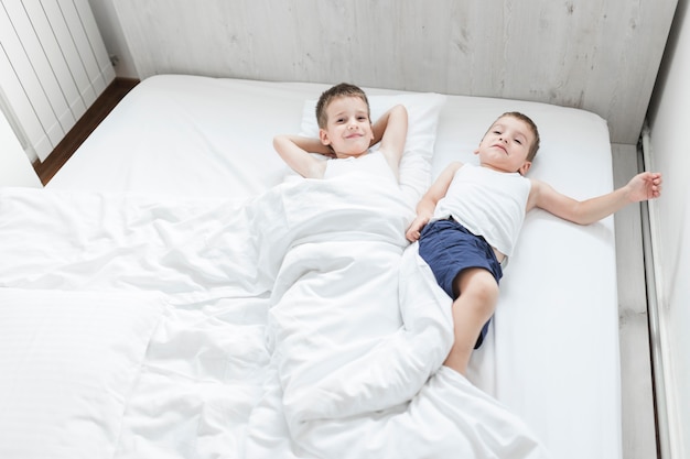 High angle view of two brothers lying on bed