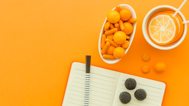 High angle view of various candies and lollipops with notepad and pen on orange surface