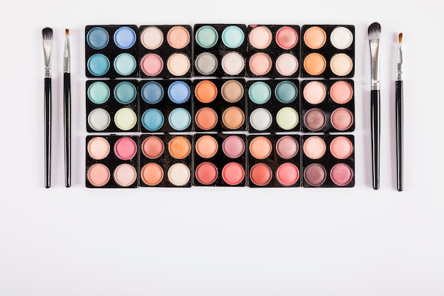 High angle view of various eye shadow powders and brushes on white background