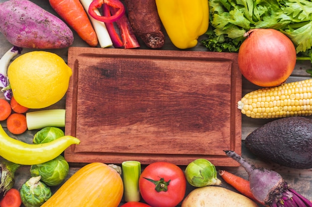 High angle view of various fresh vegetables surrounding chopping board