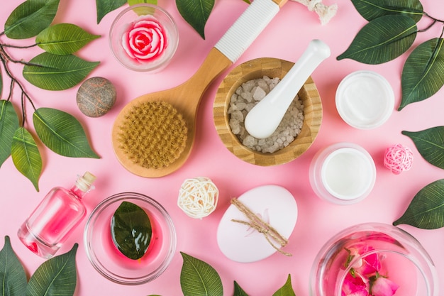 High angle view of various spa products and green leaves on pink background