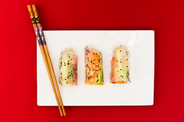 High angle view of vegetable rice spring rolls decorated with sesame seeds on white plate with wooden chopsticks