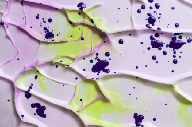 High angle view of violet watercolor drops on yellow and pink creamy textured foam surface