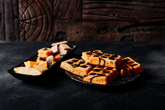 High angle view waffles in plate with cookies, orange on black textured and wooden background. horizontal