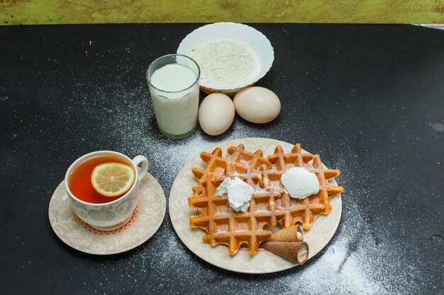 High angle view waffles in plate with tea, eggs, flour, milk on dark. horizontal