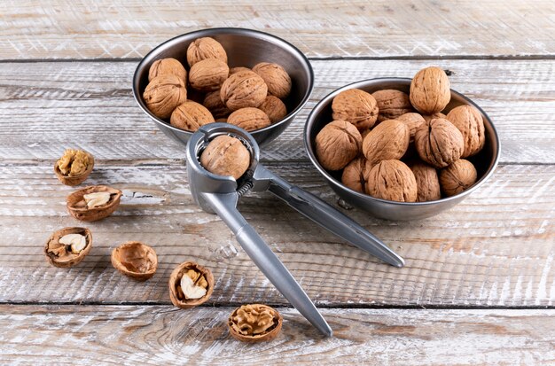 High angle view walnuts in bowls with nutcracker on wooden horizontal