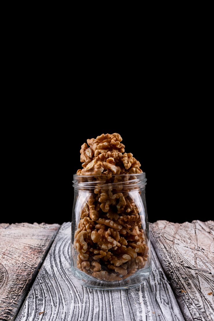 Free Photo high angle view walnuts in jar on wooden table vertical