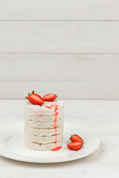 High angle view white rice cakes on plate with strawberries on white wooden board surface. vertical free space for your text