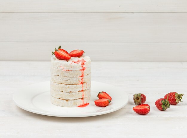 High angle view white rice cakes on plate with strawberries on white wooden board surface.