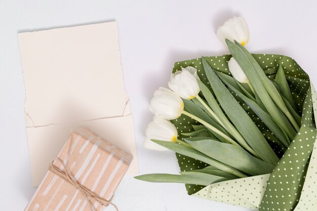 High angle view of white tulip flowers bouquet; gift box with blank paper on white background