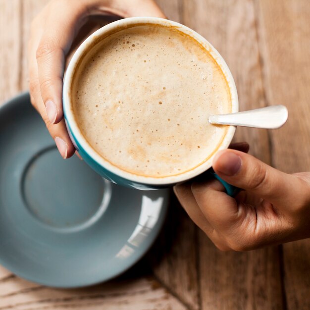 Взгляд высокого угла руки женщины держа кофейную чашку с пенистой пеной