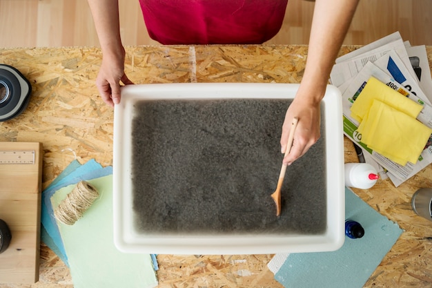 High angle view of a woman's hand stirring paper pulp in tray