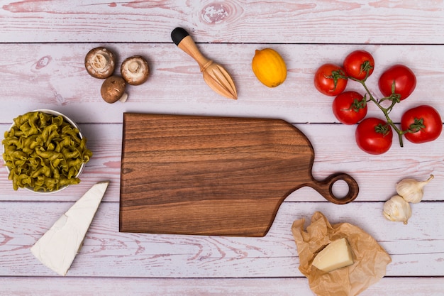 Free photo high angle view of wooden chopping board surrounding by raw pasta and ingredient on table