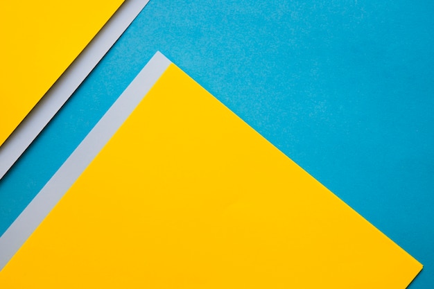 High angle view of yellow and grey cardboard papers on blue backdrop