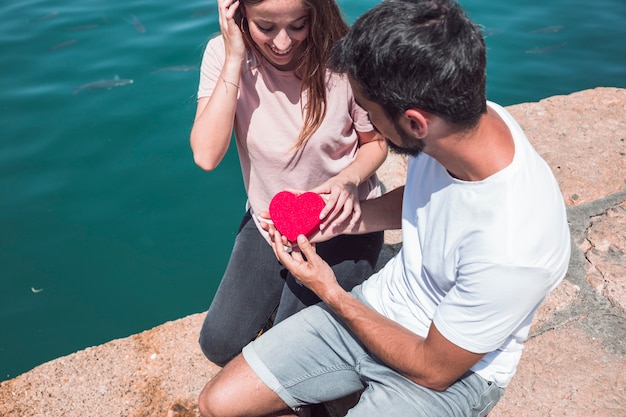 Foto gratuita la vista dell'angolo alto di giovani coppie che tengono il cuore rosso modellano vicino al mare