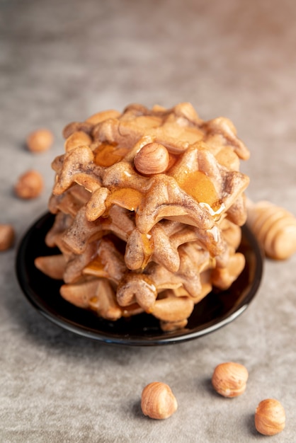 Free photo high angle of waffles stacked on plate with honey and hazelnuts