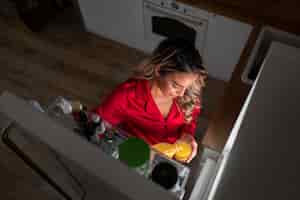 Free photo high angle woman checking fridge at night