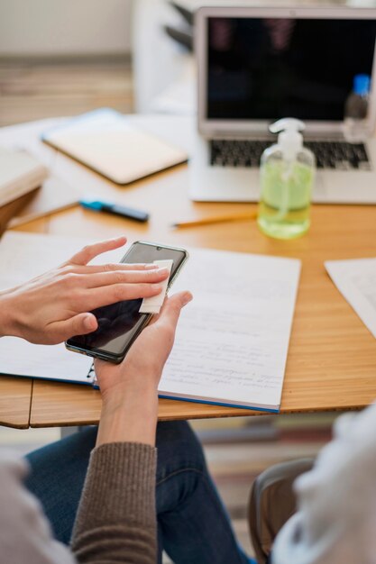 High angle of woman disinfecting her smartphone before class