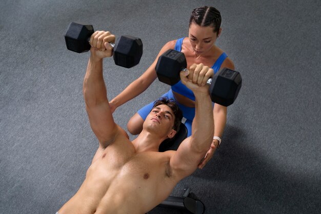 High angle woman helping man train at gym