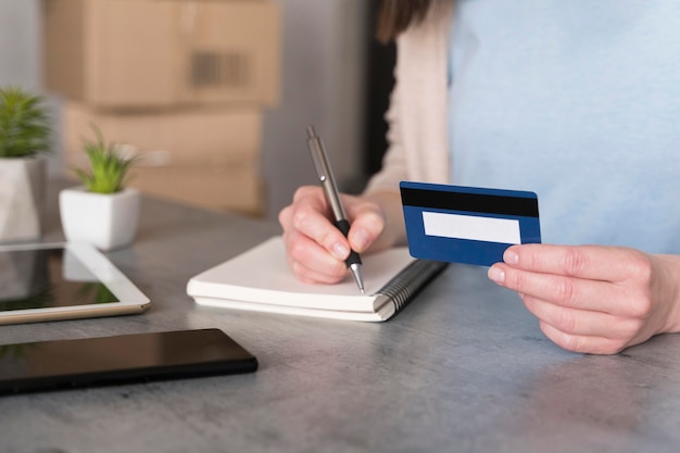 High angle of woman holding credit card and writing on notepad